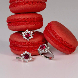 Women’s rhodium-plated silver ring with red ruby-cut cubic zirconia and floral halo design, displayed with red macarons.