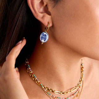 Close-up of a person wearing a gold earring with a blue and white design.