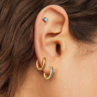 Gold hoop earrings with blue stones worn by a person with brown hair.