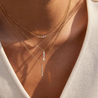 Two gold necklaces with diamond pendants on a person wearing a beige top.