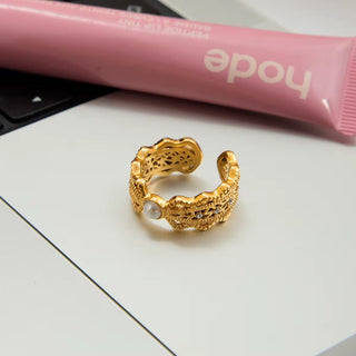Gold ring on a white surface with a pink tube in the background