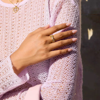 Hand wearing a gold ring on a textured pink fabric background
