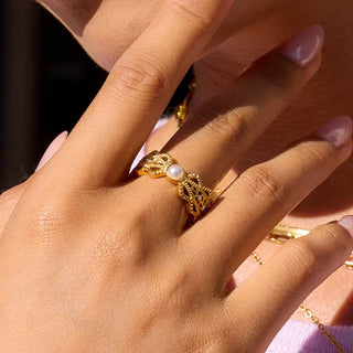 Close-up of a hand wearing a gold ring with a pearl on a blurred background