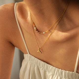 Close-up of a person wearing a gold necklace with a fish-shaped pendant.